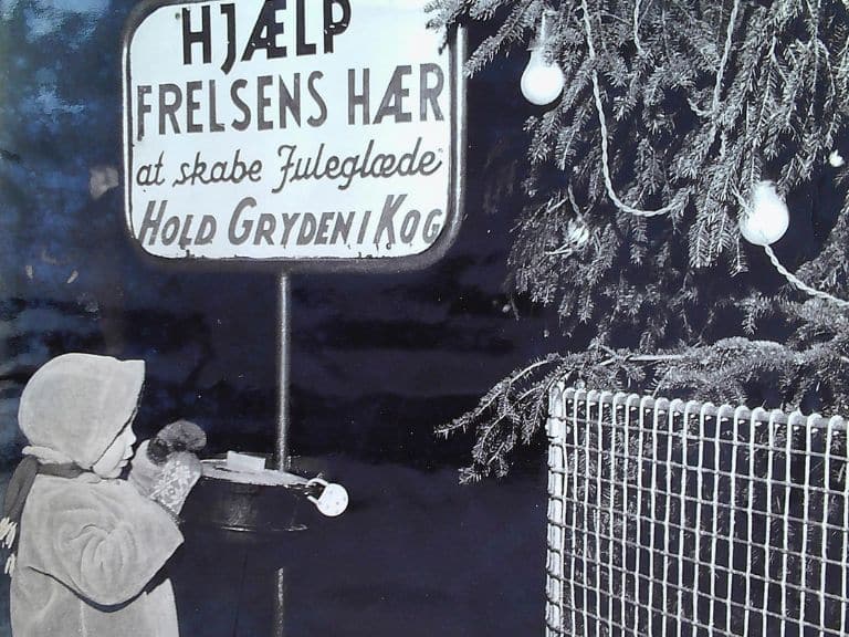 Et barn giver et bidrag i julegryden, der flankeres af byens juletræ ved indsamlingen til julehjælp i Horsens i 1961.